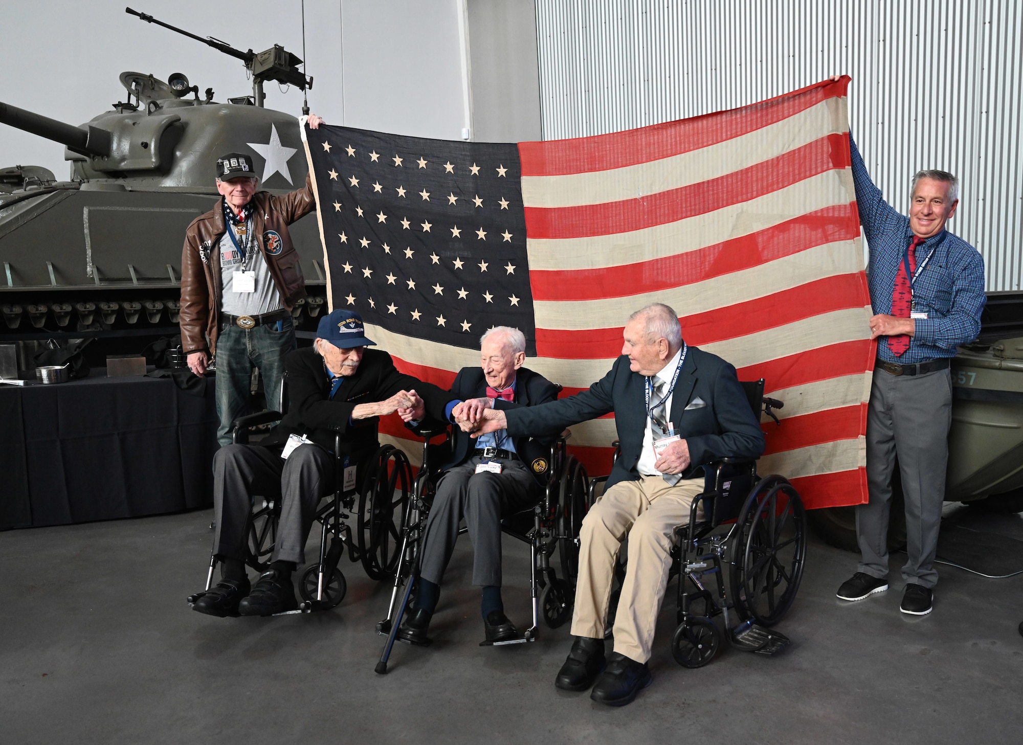 Jack O’Leary, left, and Joe O’Leary, right, hold the original 100th Bomb Group flag flown when the airfield at Thorpe Abbotts, Norfolk, England, was turned over from the Royal Air Force to the U.S. Army Air Force July 20, 1943, as World War II veterans, left to right, 2nd Lt James Rasmussen, 349th BS; Maj. John “Lucky” Luckadoo, 351st BS, and 2nd Lt. Murray Lirette, 351st BS, show the bond between them at the 100th BG reunion, National World War II Museum, New Orleans, La., May 17, 2025. The veterans, aged 101, 103 and 101 years old respectively, shared stories of some of the experiences during World War II to the more than 360 attendees at the event. (U.S. Air Force photo by Karen Abeyasekere)
