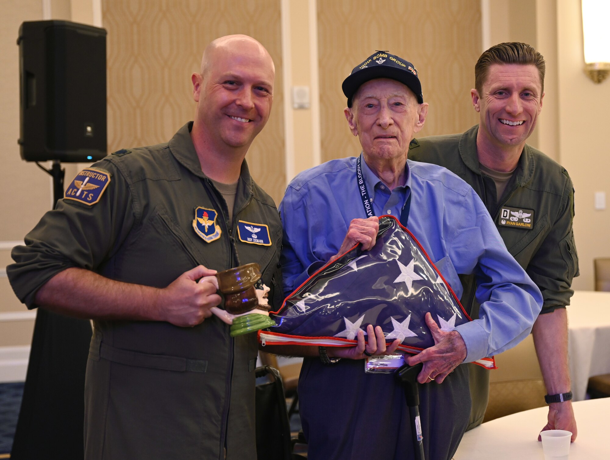 U.S. Air Force Lt Col. Matt “Indy” Ziemann, left, Department of Leadership faculty advisor, Air Command and Staff College, Maxwell Air Force Base, Alabama, and Col. Ryan Garlow, right, 100th Air Refueling Wing commander, RAF Mildenhall, England, present a flag to Maj. John “Lucky” Luckadoo, age 103, 100th Bomb Group and 351st Bomb Squadron pilot, at the 100th BG reunion in New Orleans, La., May 17, 2025. The flag was flown on a B-17 Flying Fortress and F-35 Lightning in the USA, before being hand-carried to England and being flown on 25 missions on KC-135 Stratotankers at RAF Mildenhall. Luckadoo flew 25 combat missions during World War II out of Thorpe Abbotts, Norfolk, England. (U.S. Air Force photo by Karen Abeyasekere)