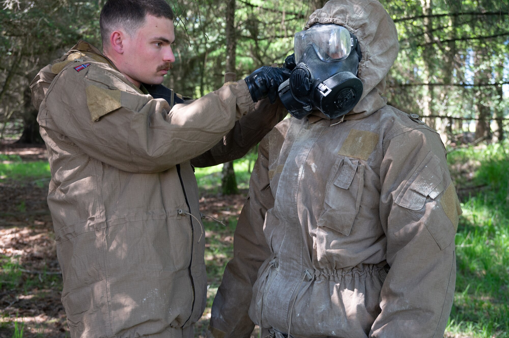 Royal Norwegian Navy Leading Seaman Forland Magnus, a force protection instructor, assists a U.S. Airman from the 426th Air Base Squadron with decontamination