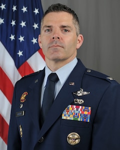 U.S. Air National Guard Col. Adam Carlson, incoming 185th Air Refueling Wing Commander, stands in front of an American flag