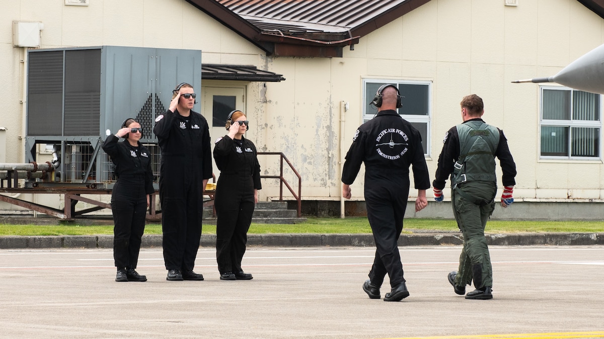 team members salute a pilot walking with another team member