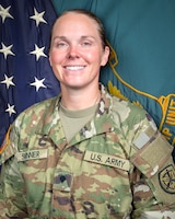 Woman in U.S. Army uniform standing in front of two flags.