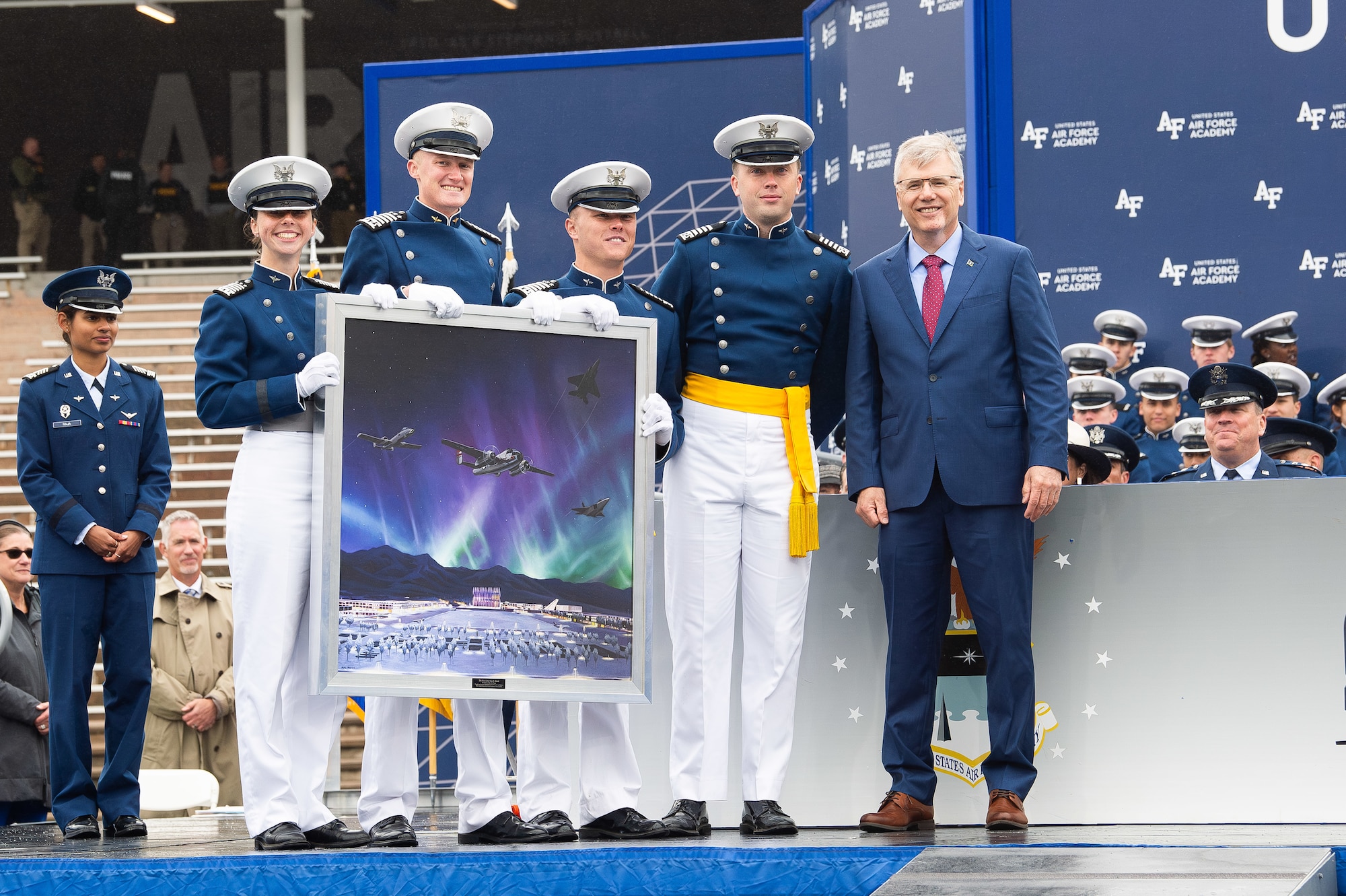 Photo of cadets from the class of 2025 posing for a photo with Secretary of the Air Force Troy Meink while holding a painting