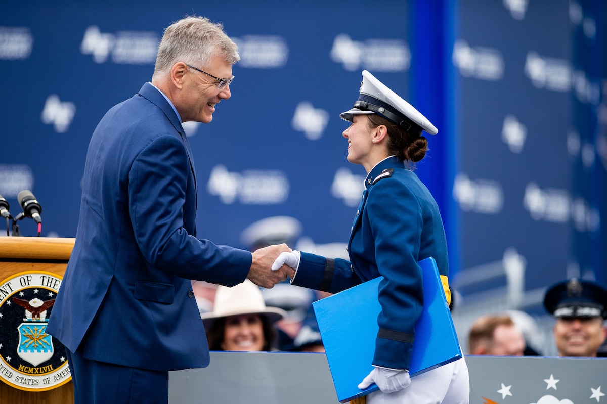 Secretary of the Air Force Troy Meink shakes a graduate's hand, while she holds her diploma