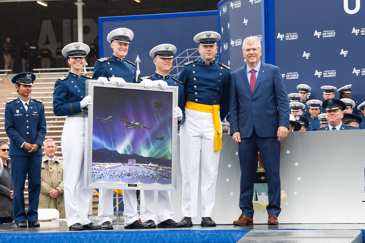 Photo of cadets from the class of 2025 posing for a photo with Secretary of the Air Force Troy Meink while holding a painting