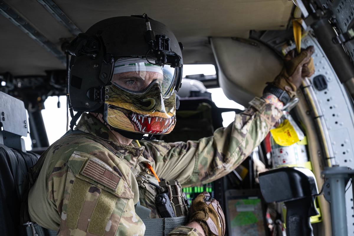 An Airman looks out of a helicopter.