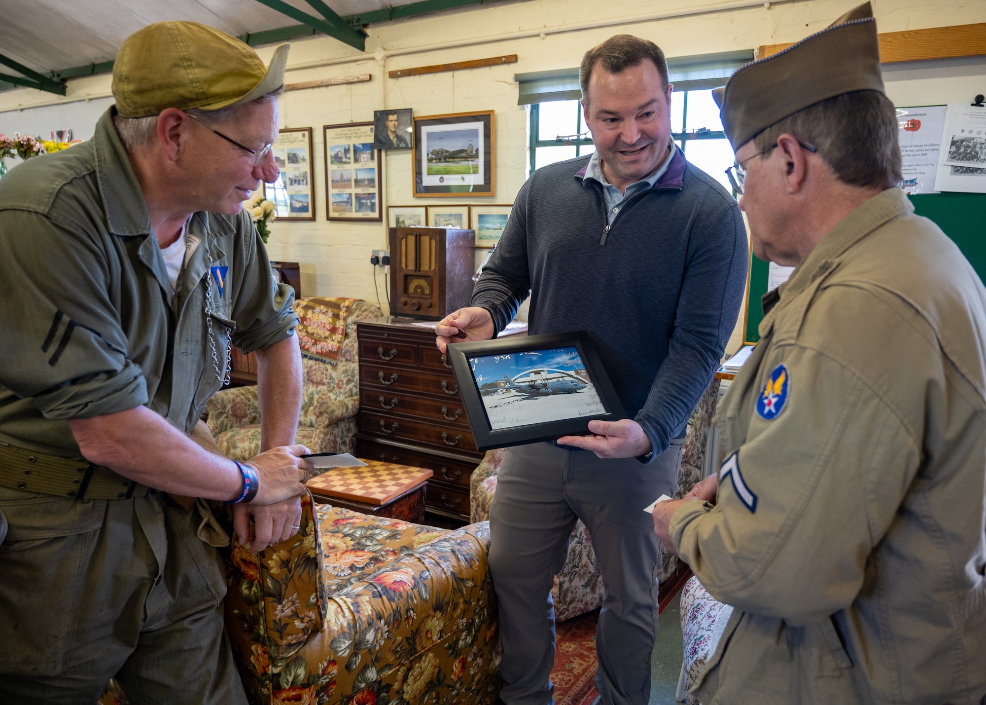 An Airman in civilian attire presents a lithograph to a museum volunteer as another man looks on