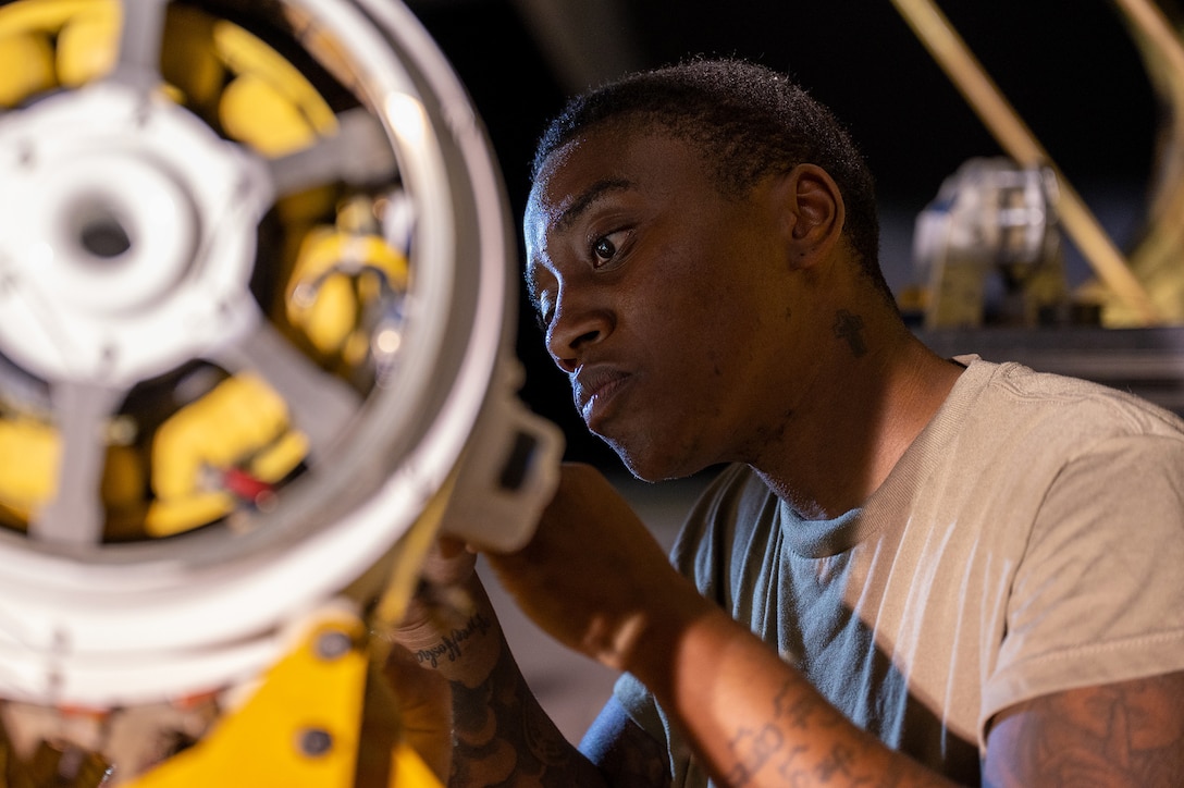 An airman looks at a yellow and silver piece of military equipment.