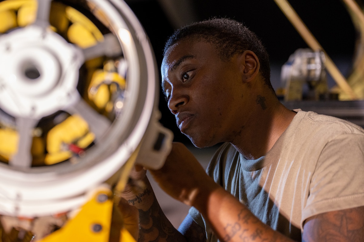 An airman looks at a yellow and silver piece of military equipment.