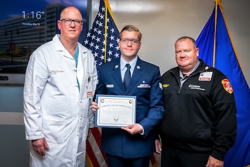 Dr Christopher Derivaux (Left) Cooper University Hospital thoracic surgeon, U.S. Air Force Senior Airman Tristan Six (Center), 87th Healthcare Operations Squadron paramedic, and Ronald Murphy Cooper (Right), University Hospital clinical manager, pose for a photo during the inaugural Air Force Paramedic Currency Platform graduation ceremony at Camden, N.J., May 22, 2025. The ceremony was held to commemorate the successful completion of the paramedic currency platform at Cooper University Hospital by two Airmen assigned to the 87th Healthcare Operations Squadron. (Courtesy photo by Avi Steinhardt)