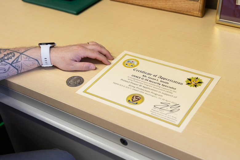 A man holds a paper certificate on top of a beige desk.