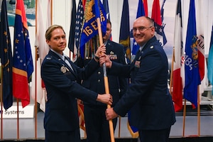U.S. Air Force Col. Candice Sperry, 350th Spectrum Warfare Group commander, left, passes the unit guidon to U.S. Air Force Lt. Col. Joseph Ellis, 16th Electronic Warfare Squadron commander, right, during the 16 EWS change of command at Eglin Air Force Base, Fla., May 28, 2025. The 16 EWS develops, tests, validates, and fields electromagnetic warfare capabilities for U.S. Air Force Global Strike assets. These capabilities enhance the survivability of warfighters and systems in contested environments. (U.S. Air Force photo by Capt. Benjamin Aronson)