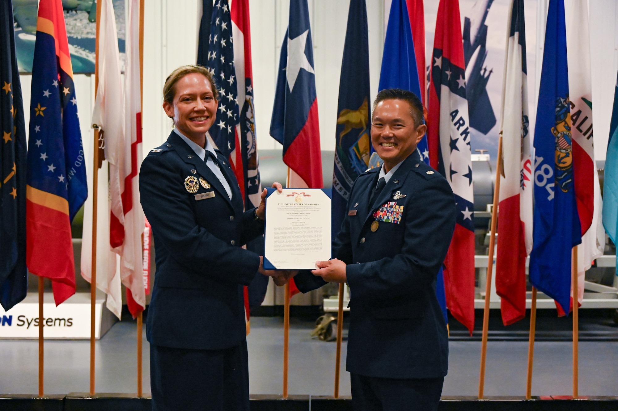 U.S. Air Force Col. Candice Sperry, 350th Spectrum Warfare Group commander, left, presents a meritorious service medal to U.S. Air Force Lt. Col. Chad Nishizuka, outgoing 16th Electronic Warfare Squadron commander, right, during the 16 EWS change of command at Eglin Air Force Base, Fla., May 28, 2025. The 16 EWS provides electromagnetic warfare support for U.S. Air Force Global Strike platforms and systems. (U.S. Air Force photo by Capt. Benjamin Aronson)