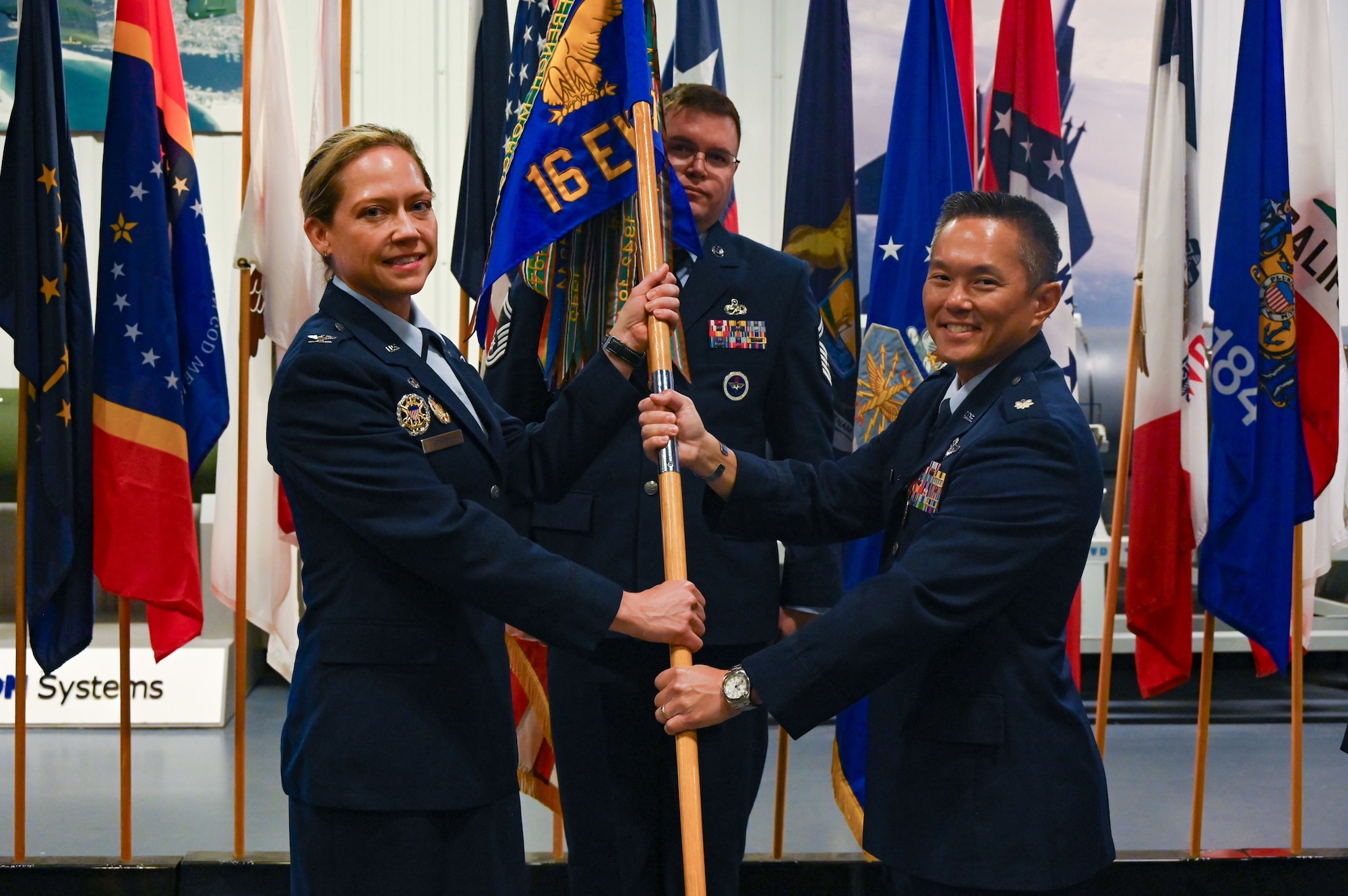U.S. Air Force Col. Candice Sperry, 350th Spectrum Warfare Group commander, left, receives the unit guidon back from U.S. Air Force Lt. Col. Chad Nishizuka, outgoing 16th Electronic Warfare Squadron commander, right, during the 16 EWS change of command at Eglin Air Force Base, Fla., May 28, 2025. The 16 EWS develops, tests, validates, and fields electromagnetic warfare capabilities for U.S. Air Force Global Strike assets. These capabilities enhance the survivability of warfighters and systems in contested environments. (U.S. Air Force photo by Capt. Benjamin Aronson)