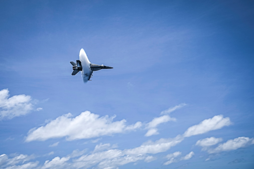 An aircraft flies in blue skies dotted with clouds.