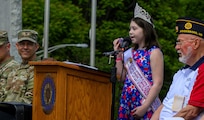 Young girl sings on stage while soldier looks on