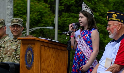 Young girl sings on stage while soldier looks on