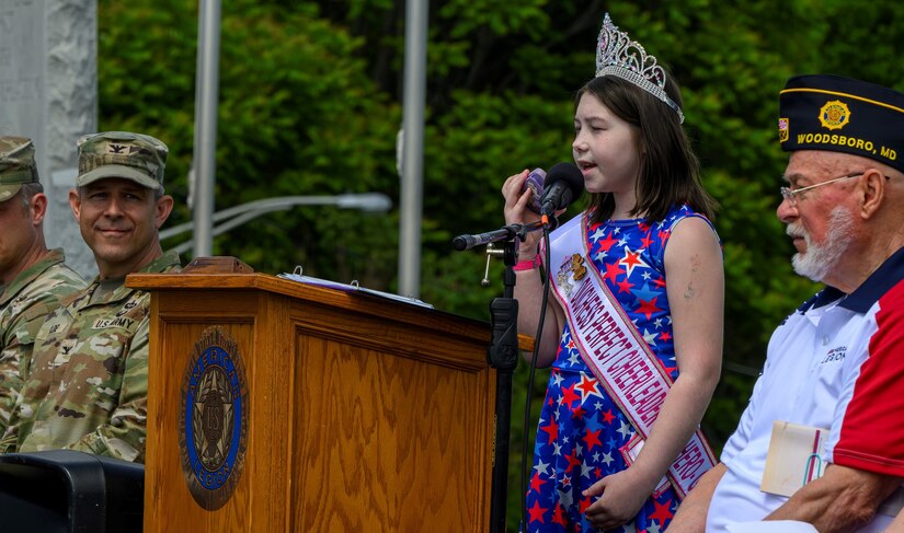 Young girl sings on stage while soldier looks on