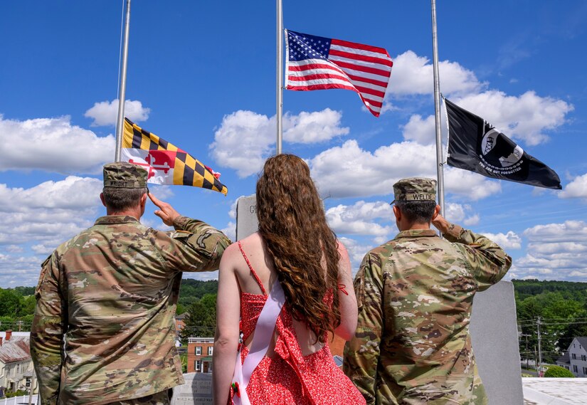 Two soldiers and a young woman salute a flag