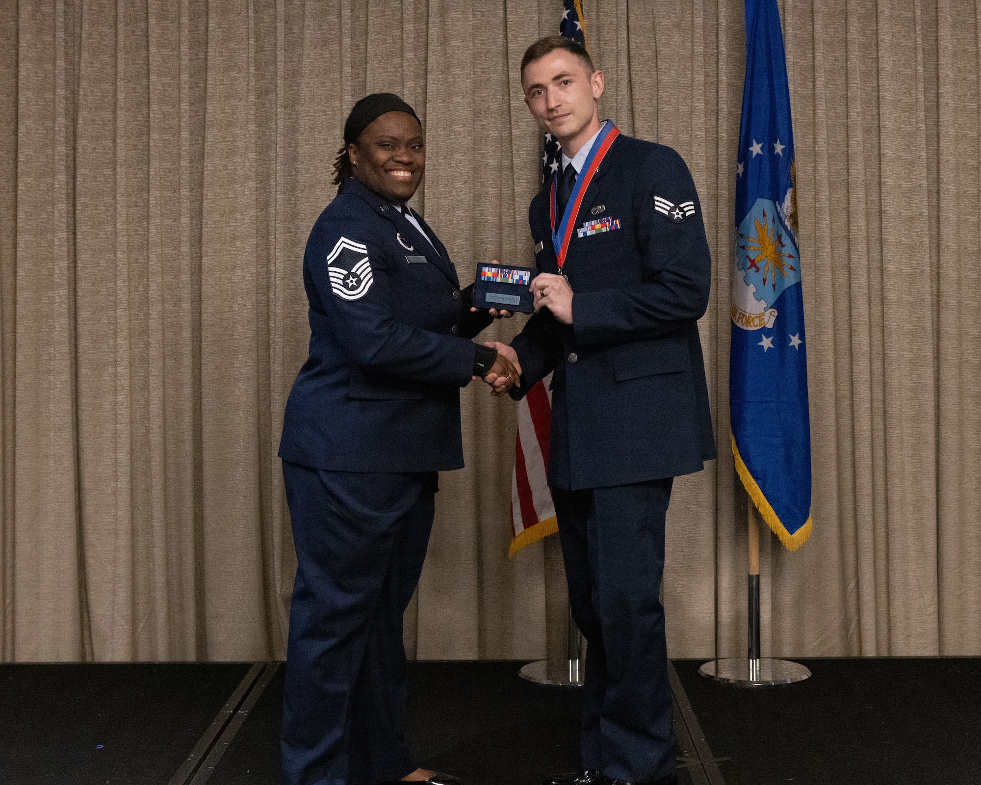 An Airman recieves an award depicting a military ribbon rack and a metal name tag with the last name, Stephensen, below it.