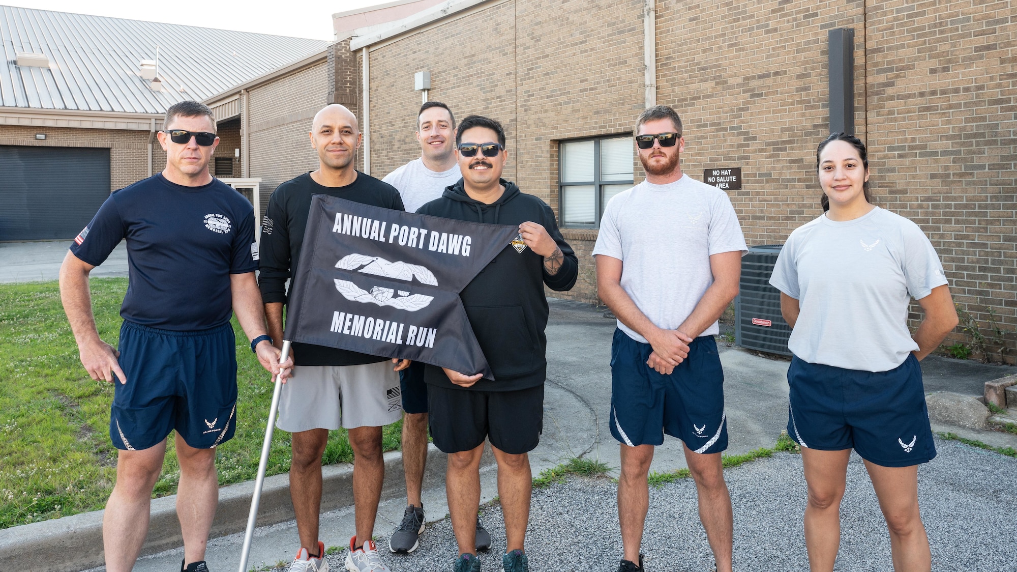 A group of people stand outside a building and hold a flag that says "Annual Port Dawg Memorial Run"