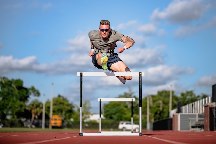 A decathlete jumps over a hurdle in a track field during a sunny day.