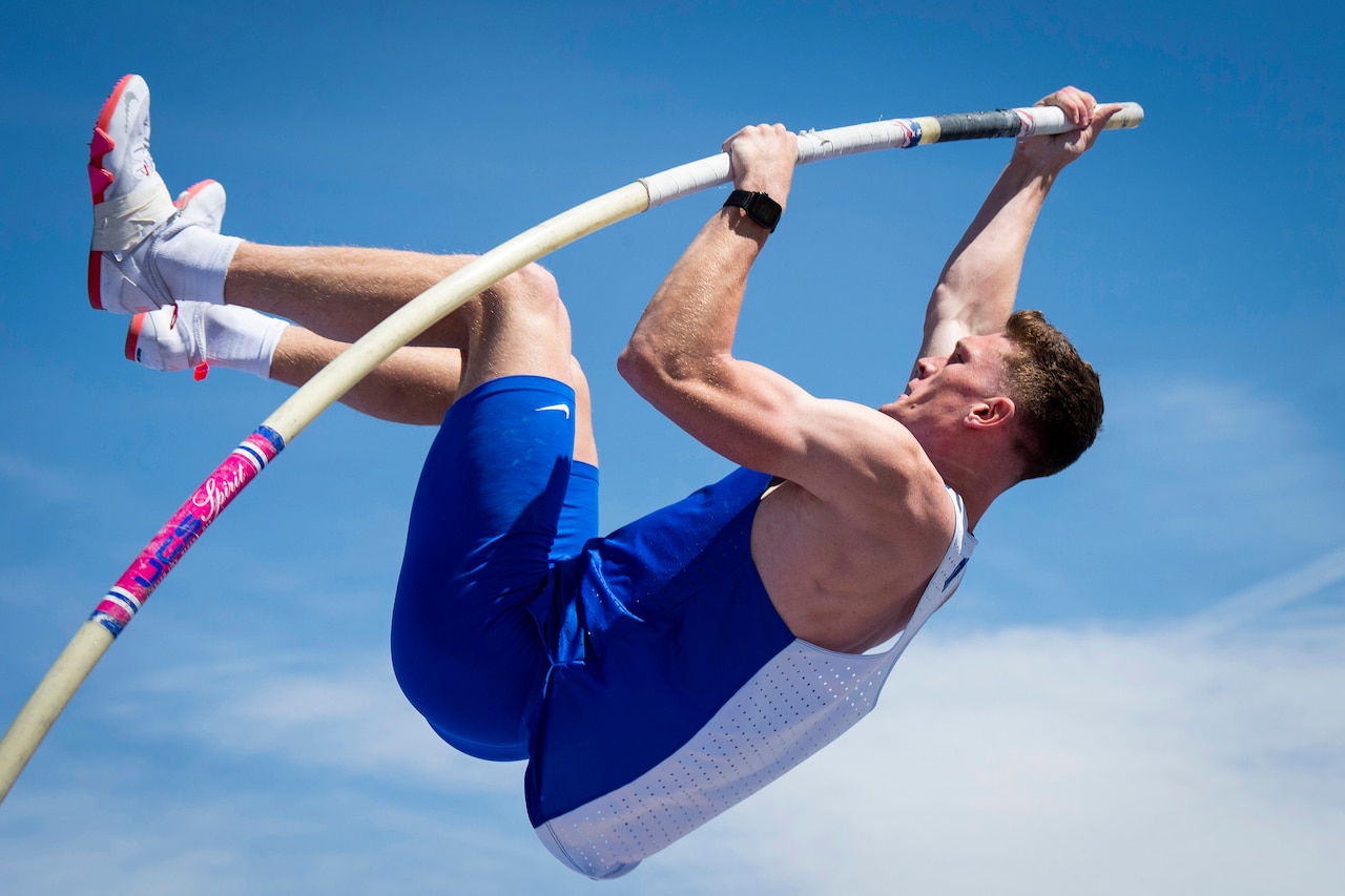 An athlete uses a pole to lift into the air with a blue sky in the background.