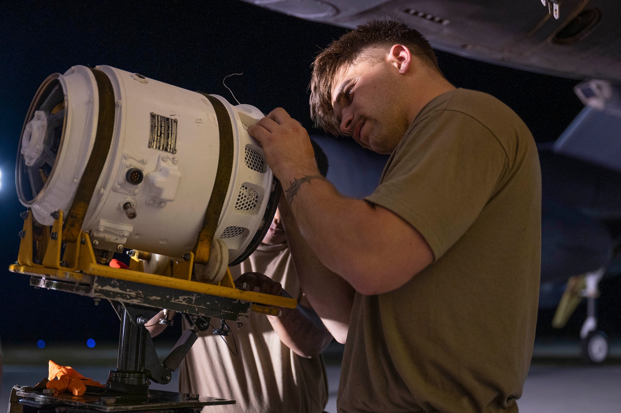 A uniformed soldier peers into a generator casing held up on a crane.