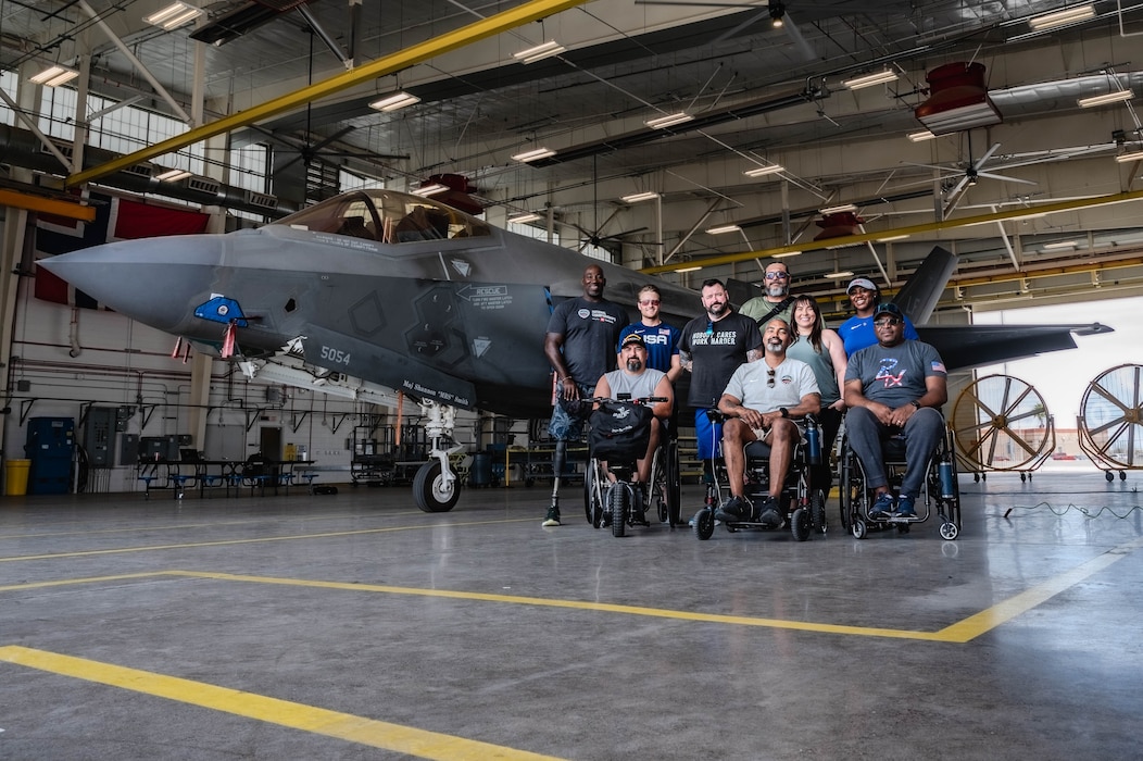 Veteran para-athletes and Team USA Coaches pose with an F-35A Lightning II aircraft during a tour of the flightline