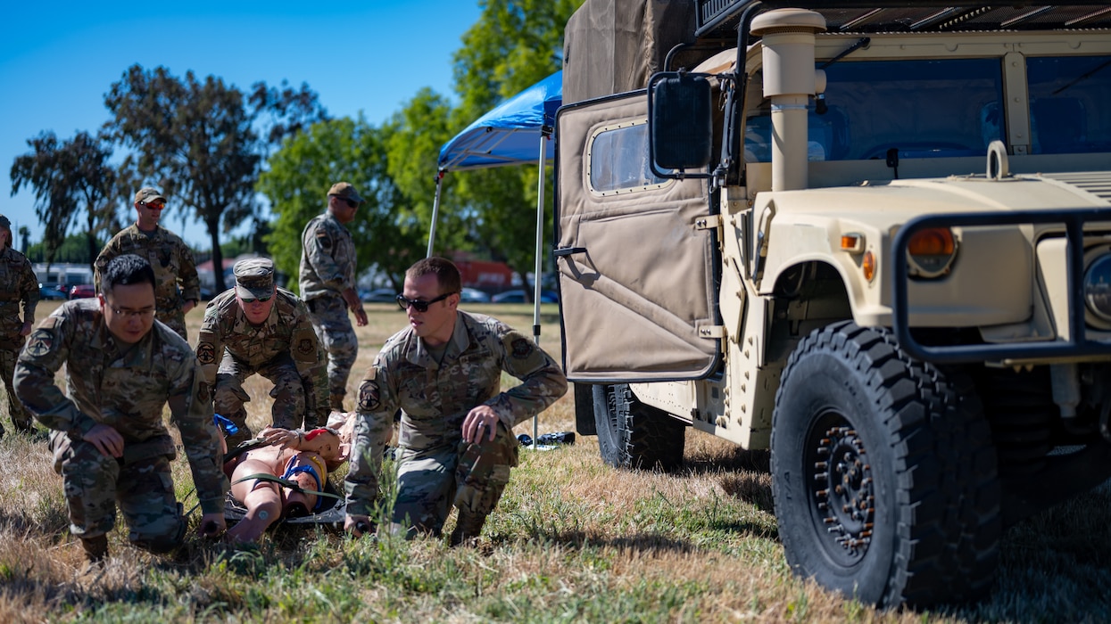 Airmen pick up a medical litter with simulated patient next to Humvee