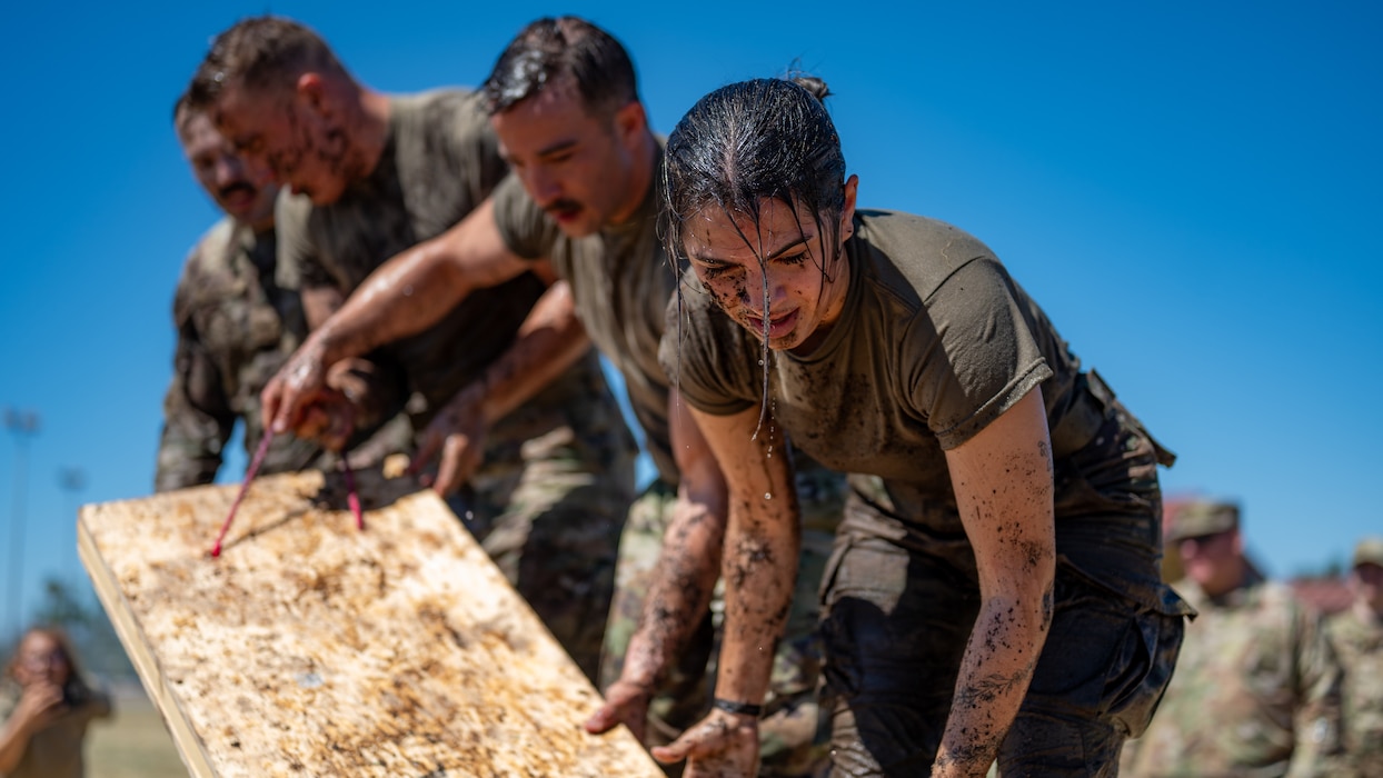 Airmen covered in mud lift a wooden plank