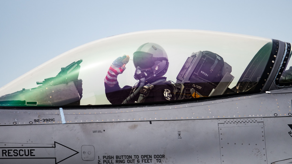 pilot inside a cockpit salutes towards out of frame person