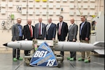 Men in suits stand behind a missile