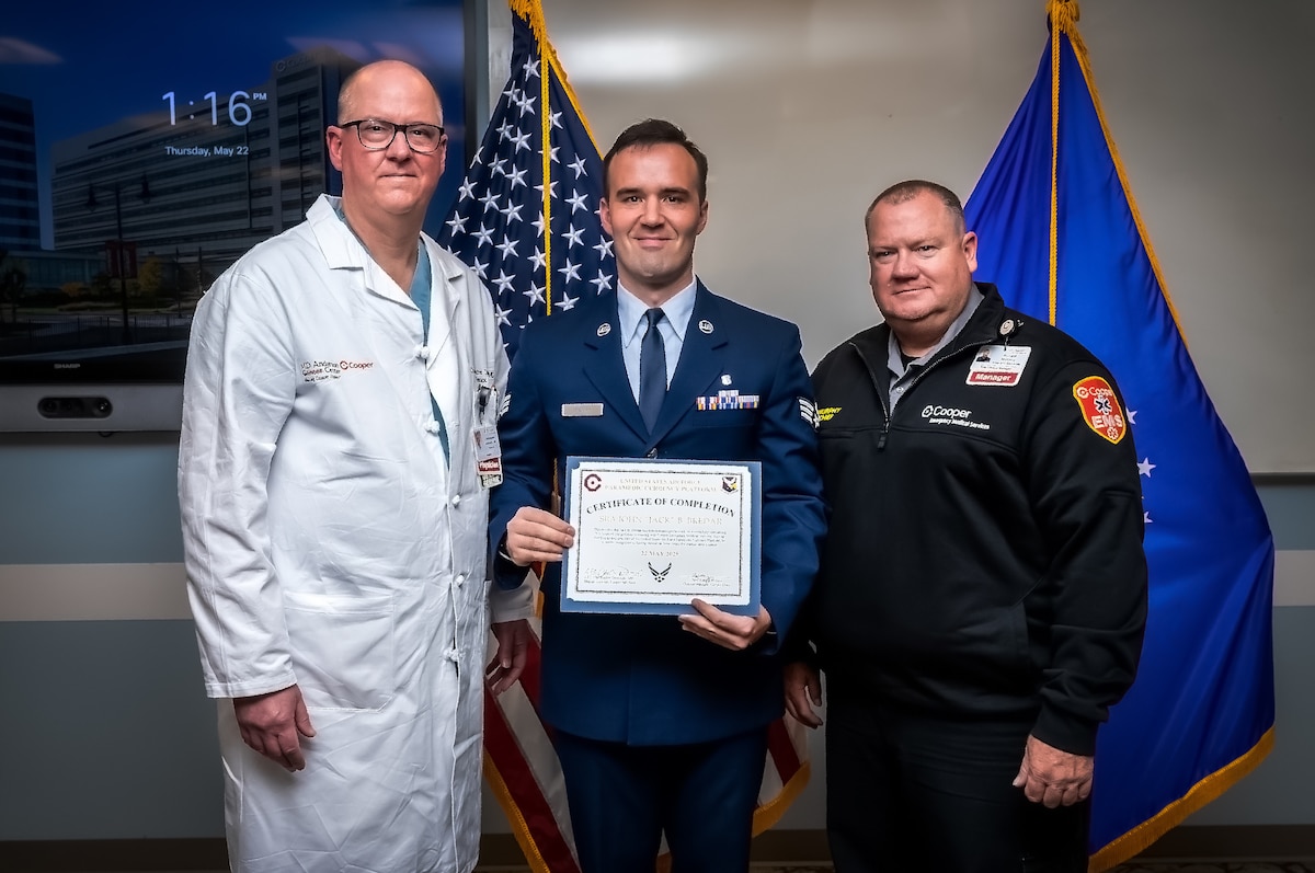 Dr Christopher Derivaux (Left) Cooper University Hospital thoracic surgeon, U.S. Air Force Senior Airman Jack Bredar (Center), 87th Healthcare Operations Squadron paramedic, and Ronald Murphy Cooper (Right), University Hospital clinical manager, pose for a photo during the inaugural Air Force Paramedic Currency Platform graduation ceremony at Camden, N.J., May 22, 2025. The ceremony was held to commemorate the successful completion of the paramedic currency platform at Cooper University Hospital by two Airmen assigned to the 87th Healthcare Operations Squadron. (Courtesy photo by Avi Steinhardt)