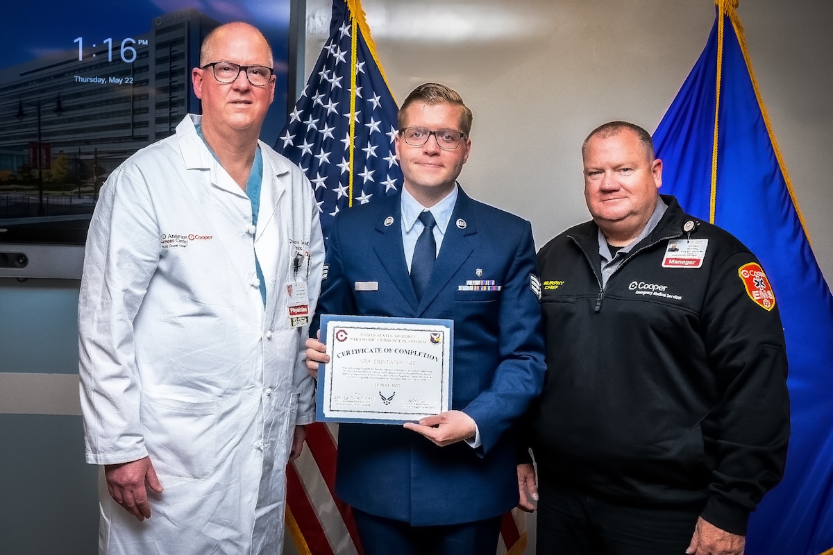 Dr Christopher Derivaux (Left) Cooper University Hospital thoracic surgeon, U.S. Air Force Senior Airman Tristan Six (Center), 87th Healthcare Operations Squadron paramedic, and Ronald Murphy Cooper (Right), University Hospital clinical manager, pose for a photo during the inaugural Air Force Paramedic Currency Platform graduation ceremony at Camden, N.J., May 22, 2025. The ceremony was held to commemorate the successful completion of the paramedic currency platform at Cooper University Hospital by two Airmen assigned to the 87th Healthcare Operations Squadron. (Courtesy photo by Avi Steinhardt)