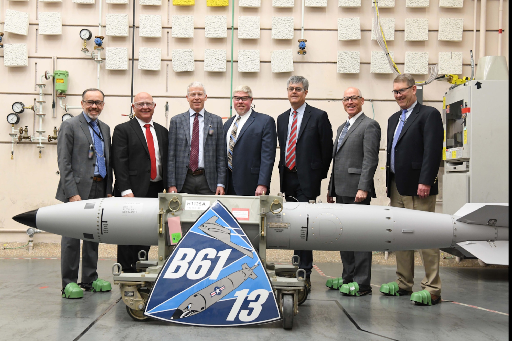 Men in suits stand behind a missile