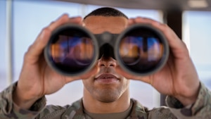 A close photo of a man looking through binoculars.