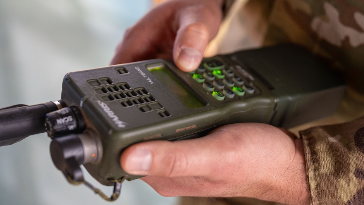 A close photo of a hand holding a radio and pressing a button.