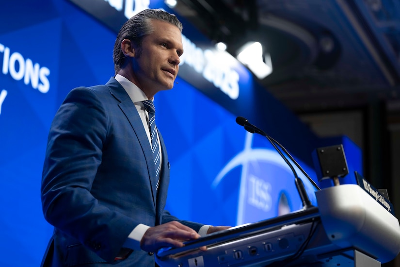 A man in a suit stands at a lectern in a podium with a blue screen in the background.