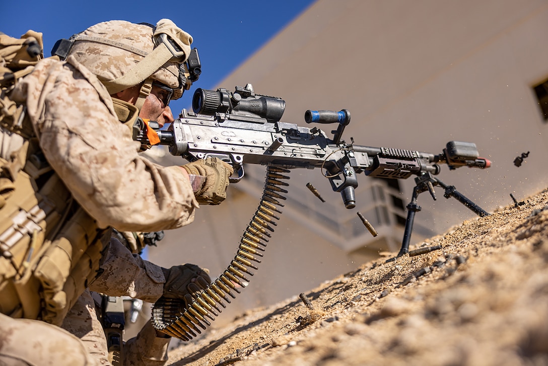 A Marine fires a machine gun while crouched in the dirt