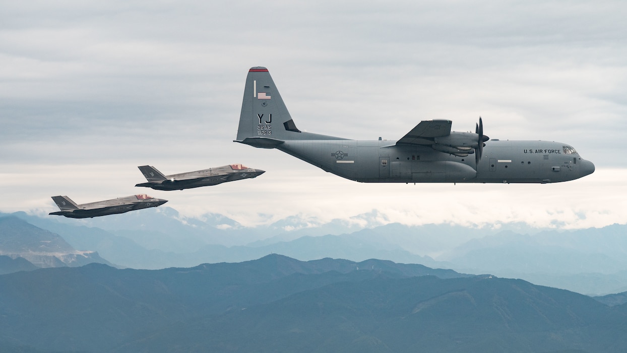U.S. Air Force C-130 cargo aircraft and F-35 fighter aircraft in a flight formation over mountainous terrain.