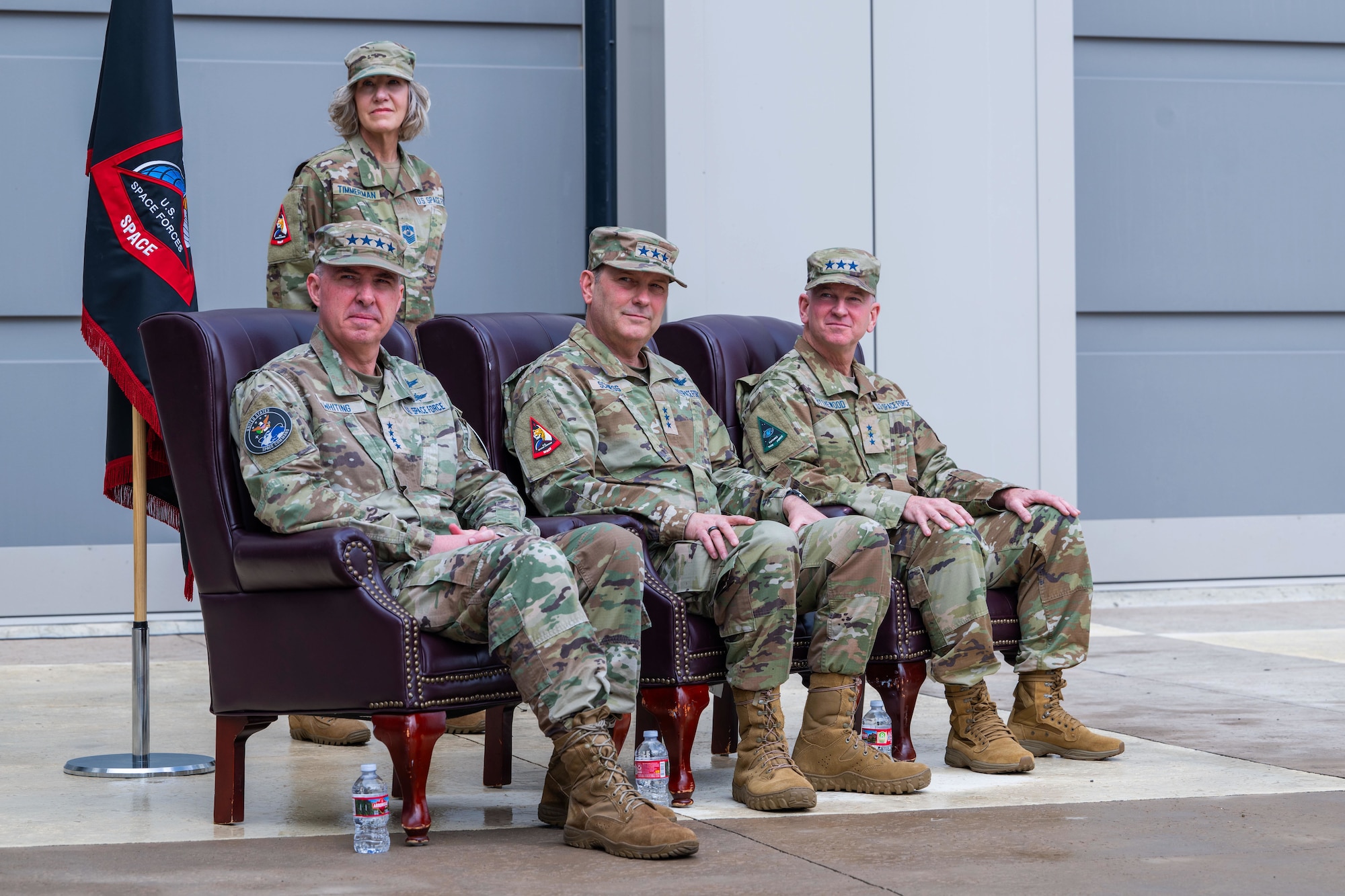 Military members sit in a row of chairs outside during a ceremony.