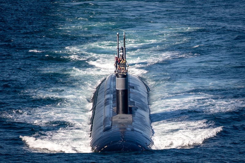 A sailor stands near the periscope of a partly submerged submarine.