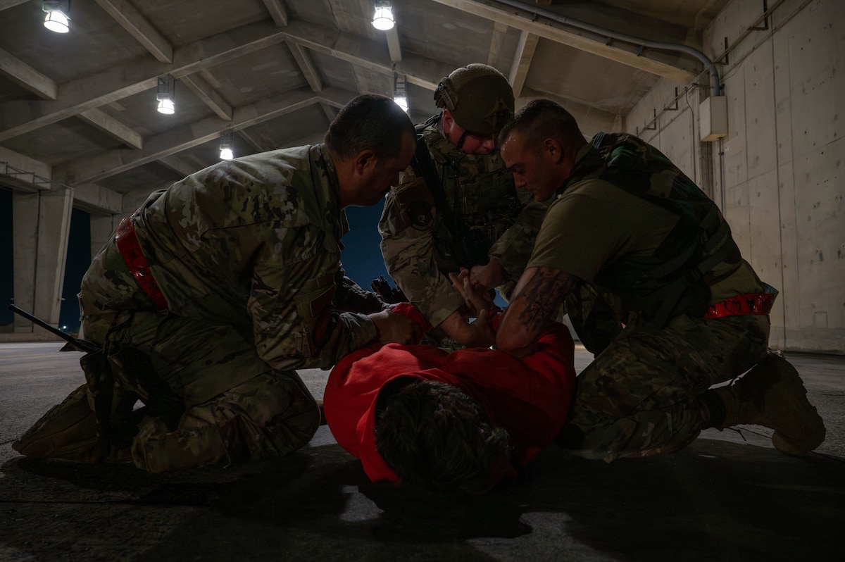 Two U.S. Air Force Airmen assigned to the 119th Expeditionary Fighter Generation Squadron detain a simulated intruder as a U.S. Air Force Airman assigned to the 18th Security Forces Squadron arrives during base-wide operational readiness exercise, BH 26-1 at Kadena Air Base, Japan, Nov. 6, 2025. The scenario tested response time and coordination between maintainers and security forces during a simulated flightline intrusion. (U.S. Air Force photo by Airman Nathaniel Jackson)