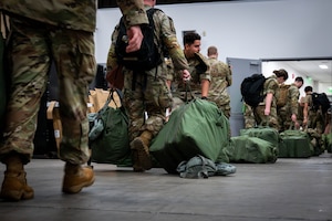 Simulated deploying personnel carry their inspected individual protective equipment bags.