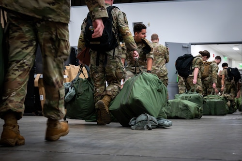 Simulated deploying personnel carry their inspected individual protective equipment bags.