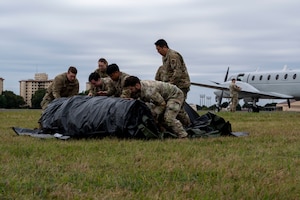 Military members unroll a green tent.