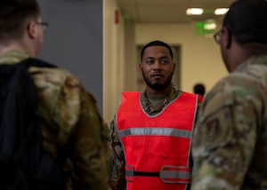 A military member in a neon orange vest speaks with two other military members.