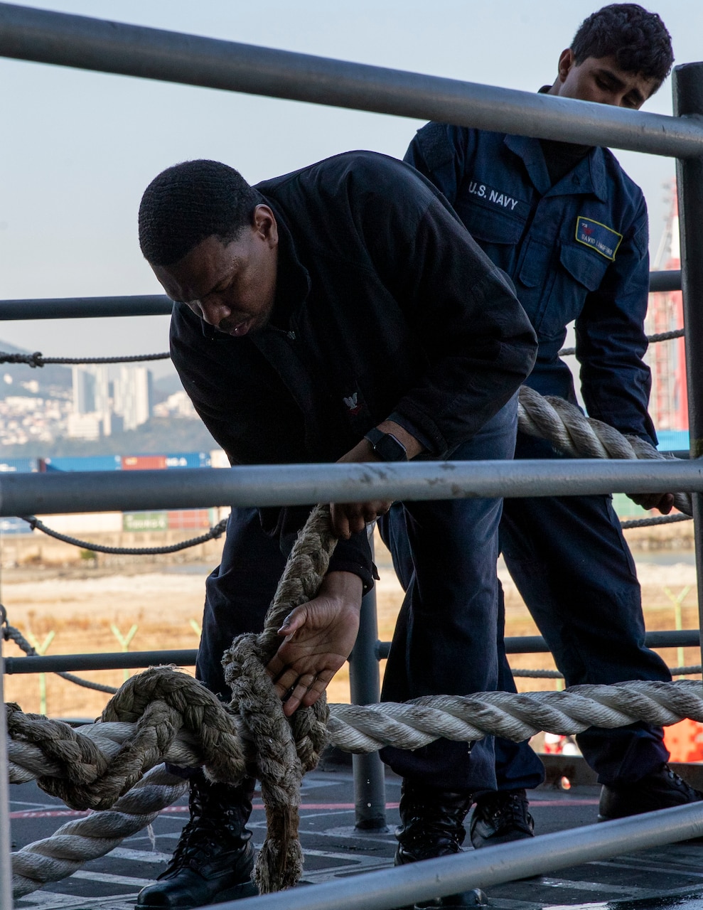 Boatswain’s Mate 2nd Class Kevin Phynon, front, and Seaman Apprentice David Langford, both from Texas and assigned to deck department, secure a mooring line on the fantail during a sea-and-anchor evolution aboard Nimitz-class aircraft carrier USS George Washington (CVN 73) while pulling into Busan, Republic of Korea, Nov. 5, 2025.