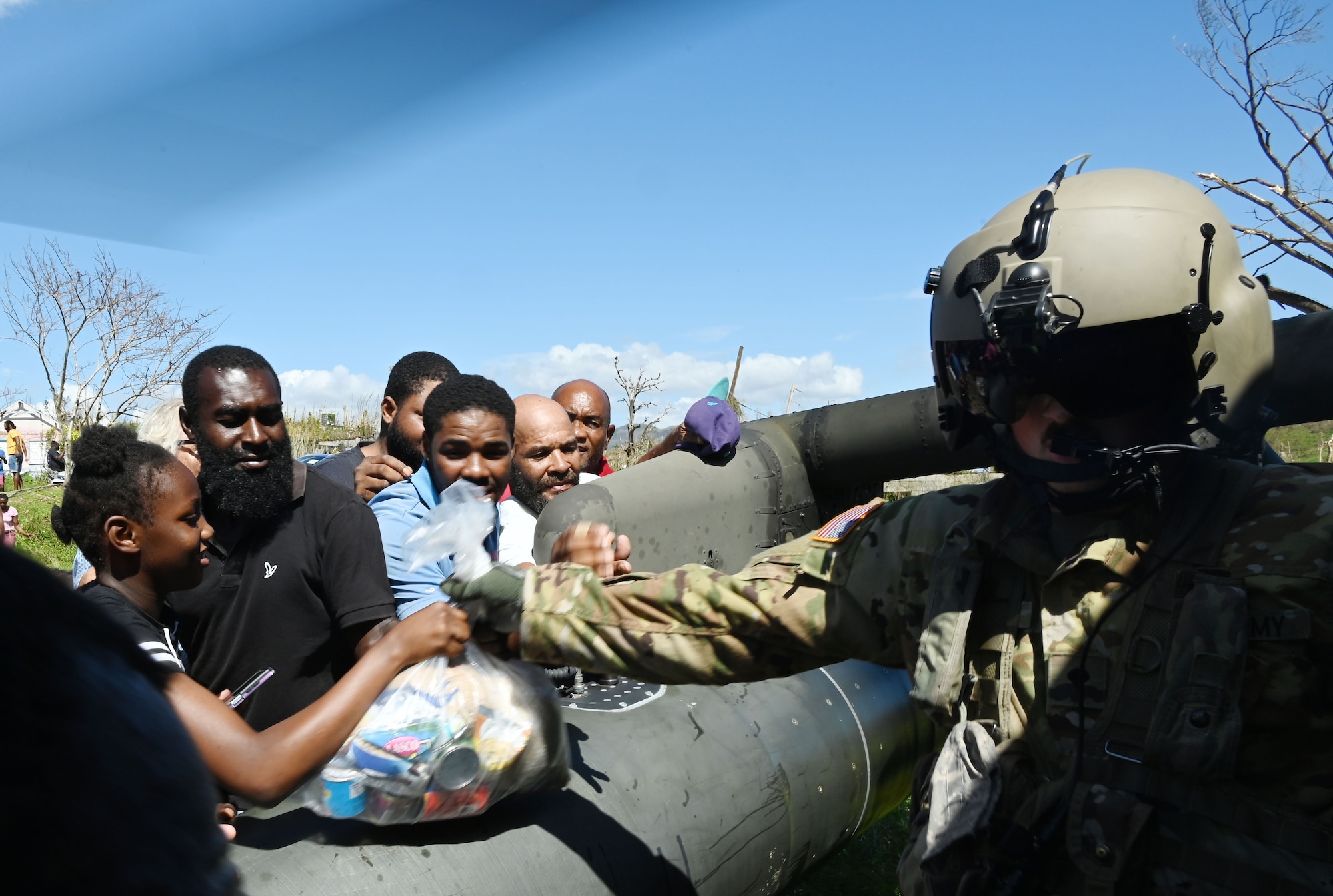 A military soldier hands out a bag of food to people.